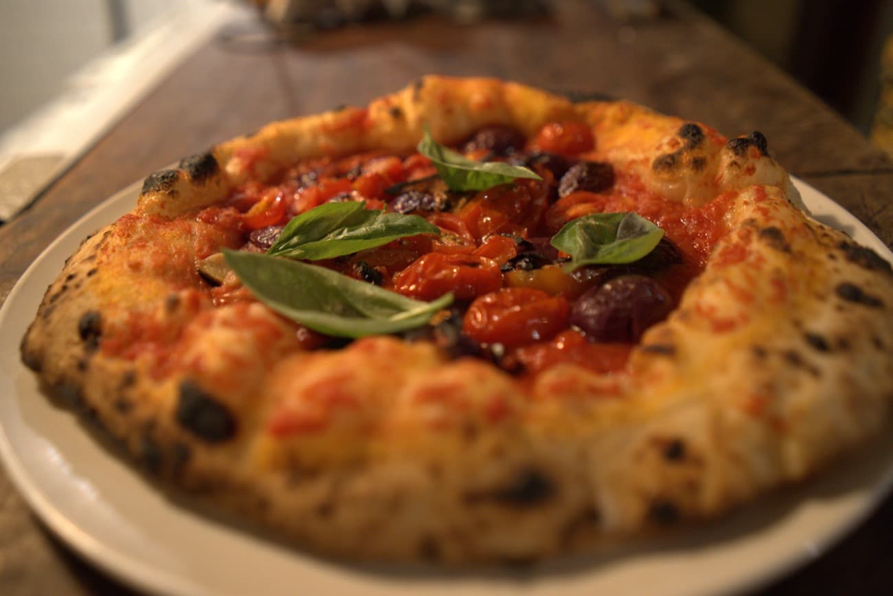 Close da borda alta e alveolada, com o molho de tomate fresco e as folhas de manjericão