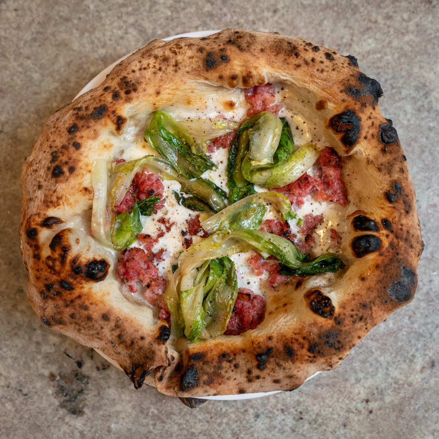 Pizza vista de cima, com a borda alta marcada de manchas de leopardo, linguiça e escarola