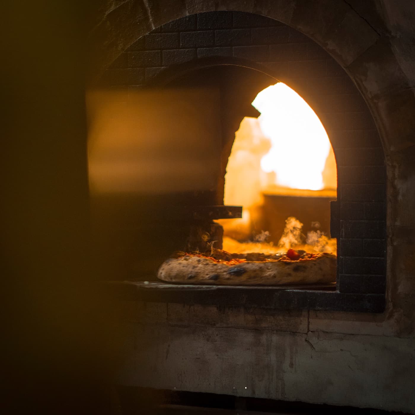 Pizza assando dentro do forno de tijolos, vista pela boca do forno